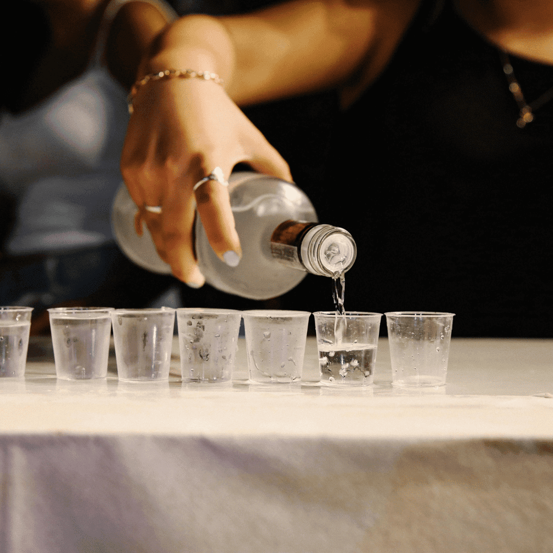 Pouring clear liquid into multiple small cups on a table.